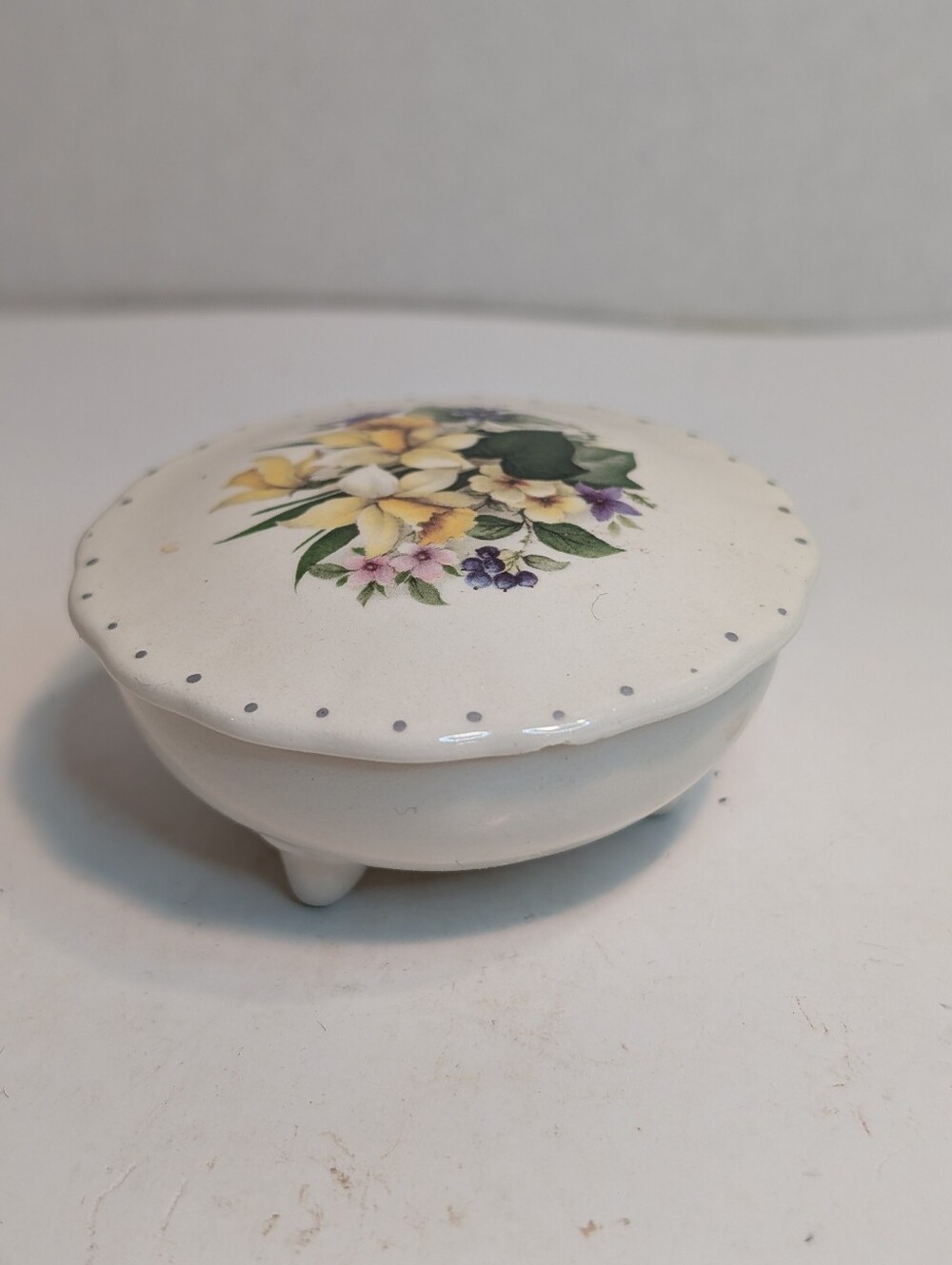 A vintage porcelain or ceramic floral trinket box with three feet and dotted rim